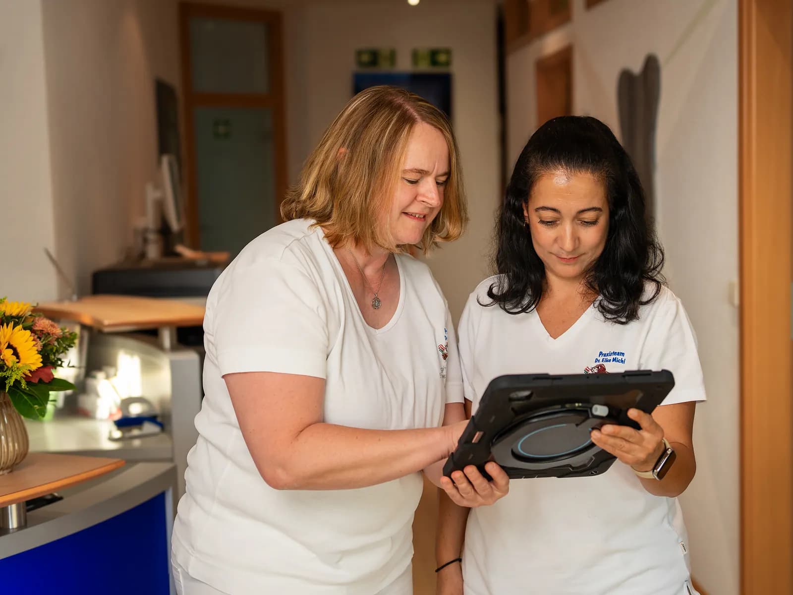 Zwei Mitarbeiterinnen stimmen sich im Flur der Praxis am Tablet ab